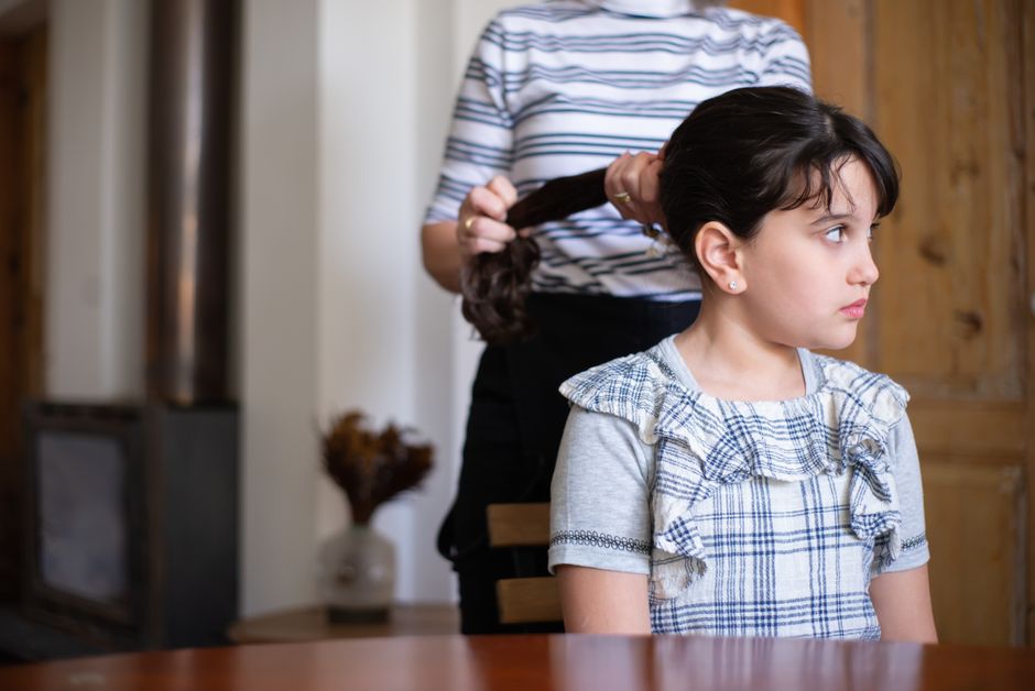 Una madre trenzando el cabello de su hija en casa, capturando un tierno momento familiar.
