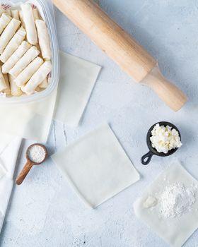Flat lay photo showcasing uncooked spring rolls with ingredients like flour and cheese on a wooden table.