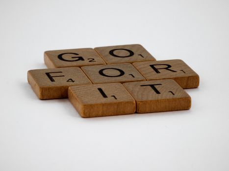 Close-up of Scrabble tiles spelling 'Go For It', inspiring motivational quote on white surface.