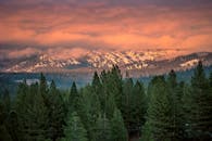 白雪皑皑的山脉、郁郁葱葱的松林和迷人的日落，映衬着充满活力的天空