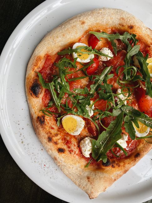 Enjoy this mouthwatering homemade pizza topped with arugula and eggs on a white plate.