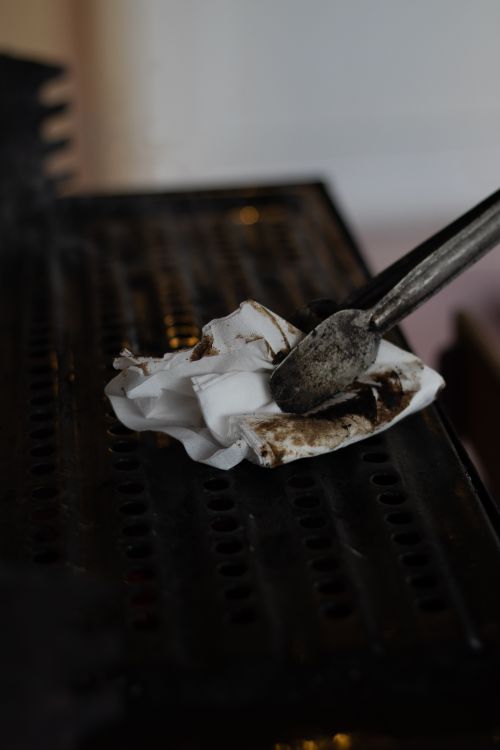 Free Close-up of tongs using a dirty tissue to clean a grill grate, emphasizing hygiene. Stock Photo