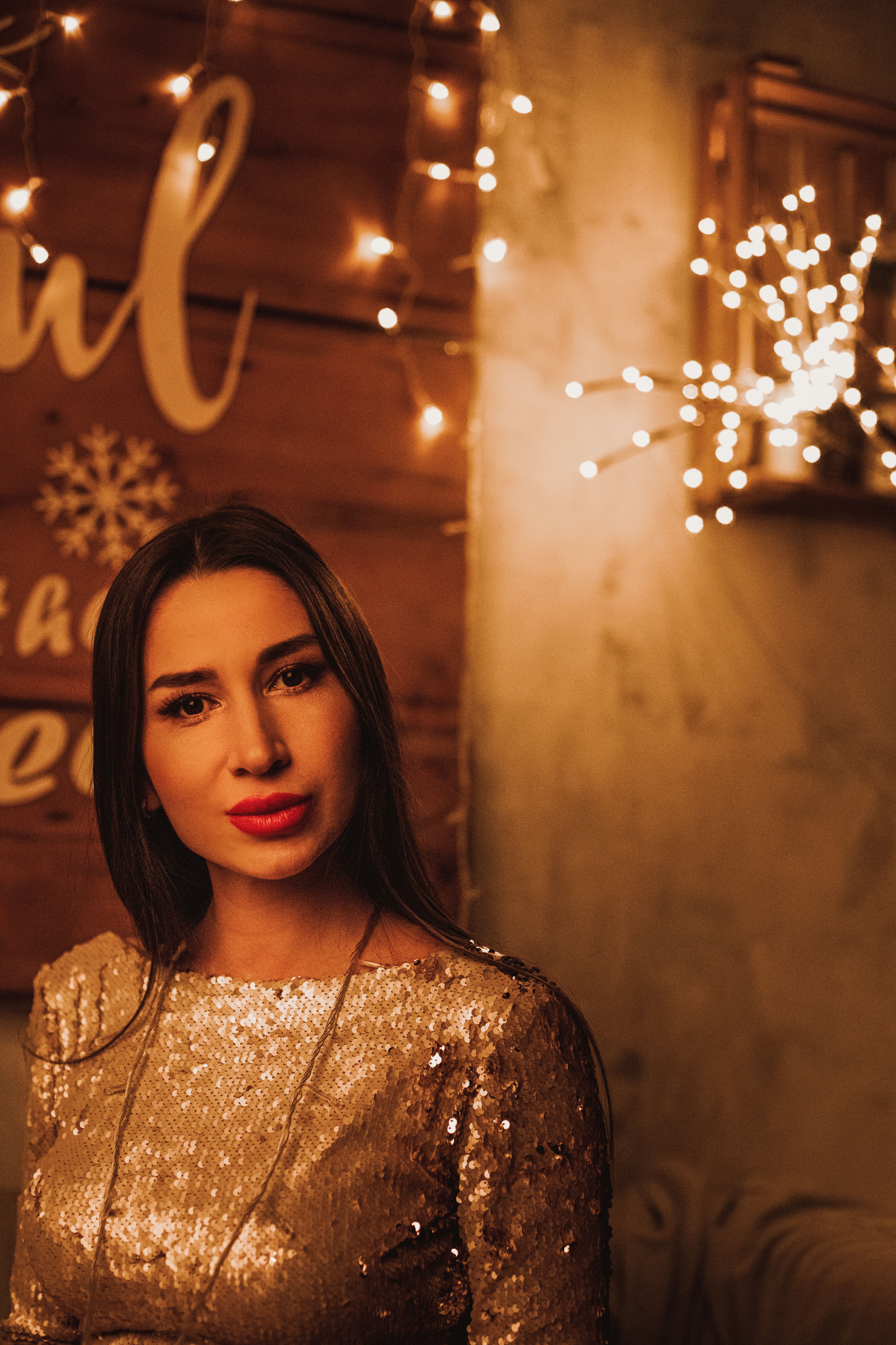 Portrait of a woman in a sparkling dress with warm festive lights, creating a cozy holiday atmospher