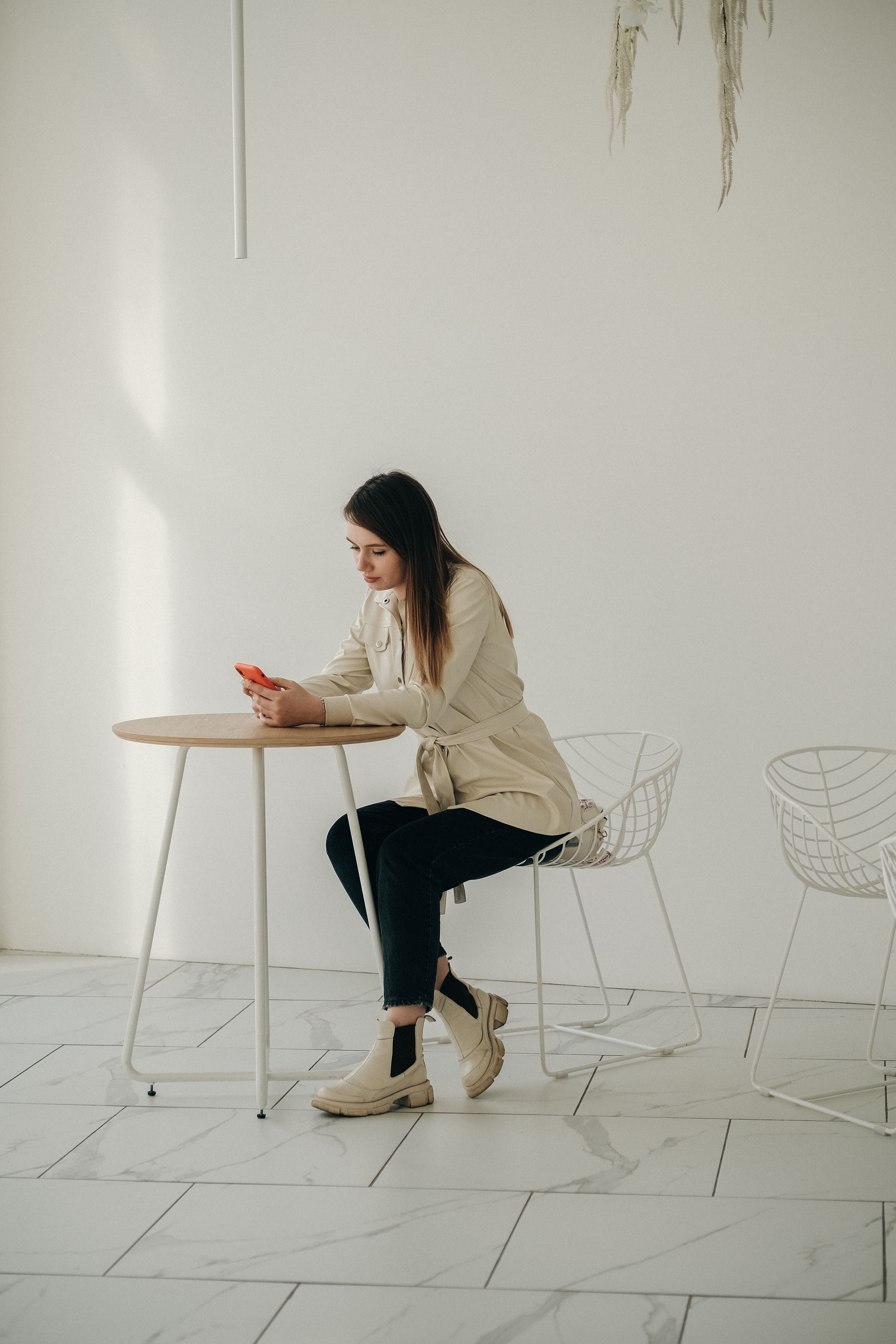 Side view of thoughtful woman in casual clothes sitting at light table and using smartphone in cafe in minimalistic style in daytime