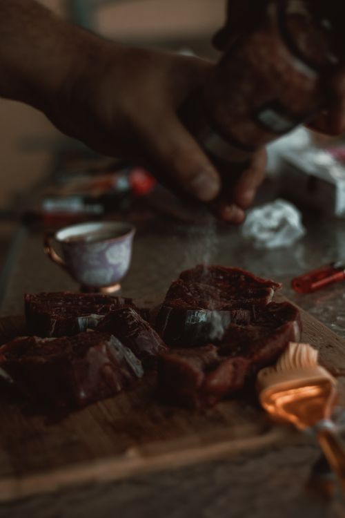 Free Close-up of hands seasoning raw meat on a wooden board, with brush and spices. Stock Photo