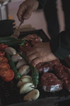 Close-up of hands grilling meat and vegetables. Ideal for BBQ and cooking themes.