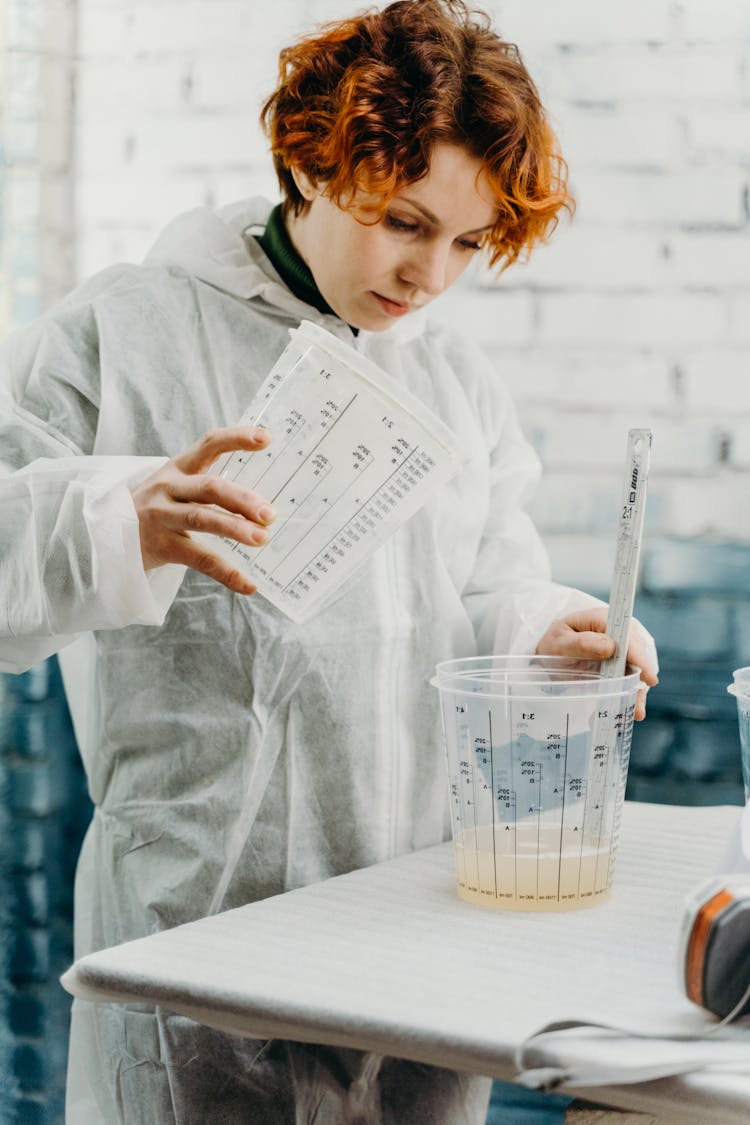 A Woman In Coveralls Mixing Paint In A Bucket