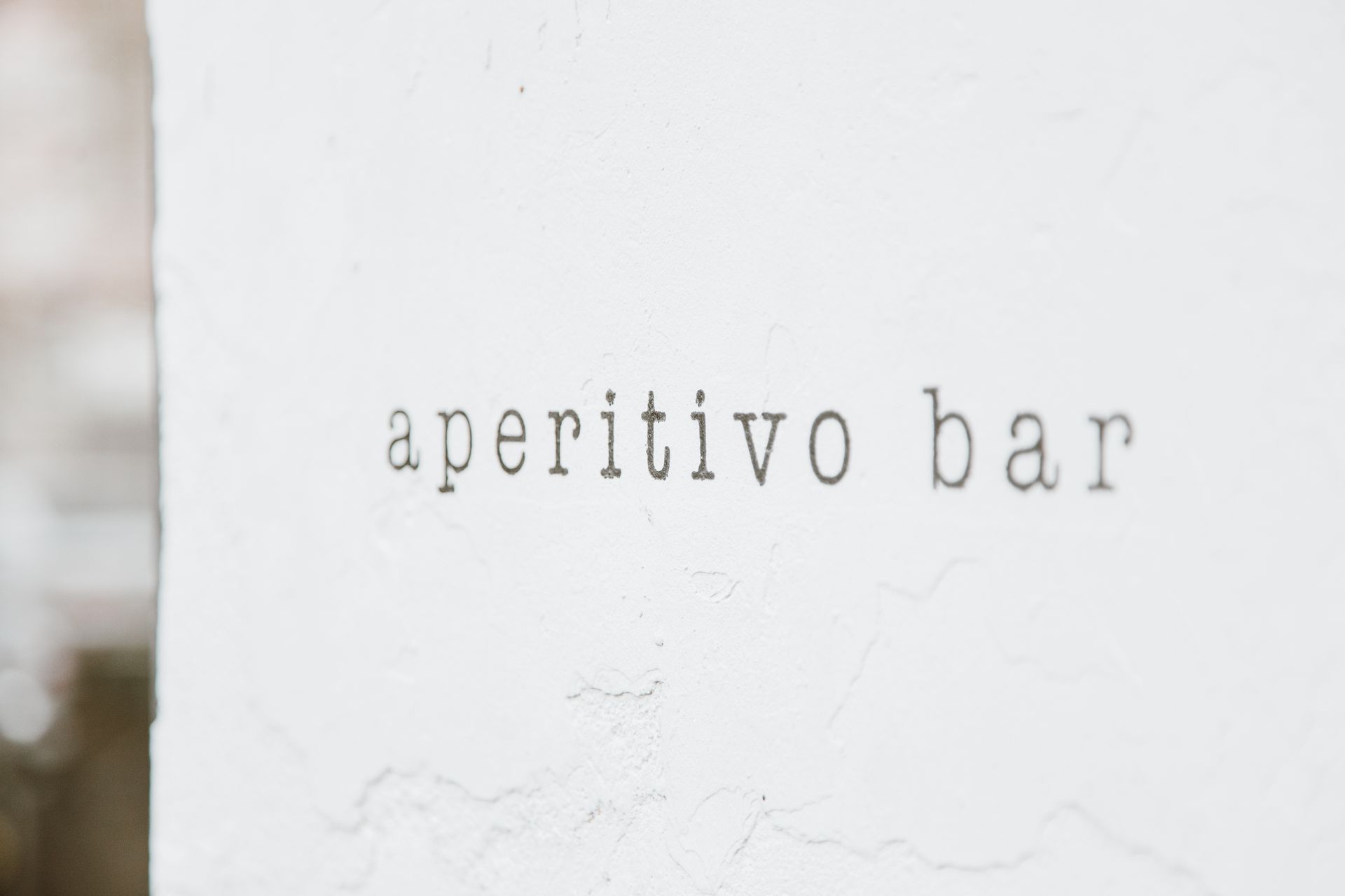 A minimalist image showing the text 'aperitivo bar' on a textured white wall, ideal for modern decor.
