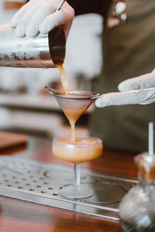 Free Bartender expertly pours a crafted cocktail through a strainer into a glass. Stock Photo