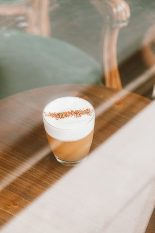 Free A frothy coffee drink served in a glass on a wooden table, viewed through a window. Stock Photo