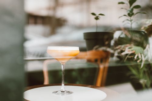 Free Stylish cocktail glass on a table by the window with plants in the background. Stock Photo