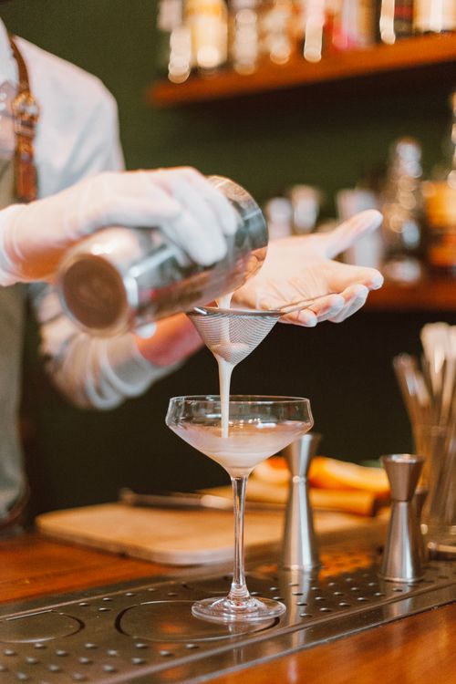Free Bartender pouring a creamy cocktail through a strainer into a glass at a bar. Stock Photo