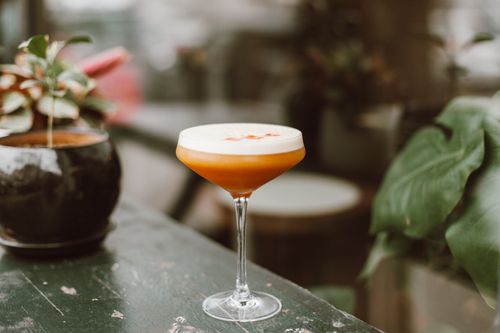 Free A stylish cocktail on a table surrounded by green foliage, creating a serene ambiance. Stock Photo