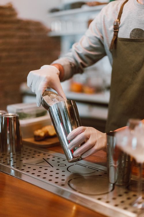 Free Bartender skillfully mixing drinks with an ice-filled shaker in a modern bar atmosphere. Stock Photo