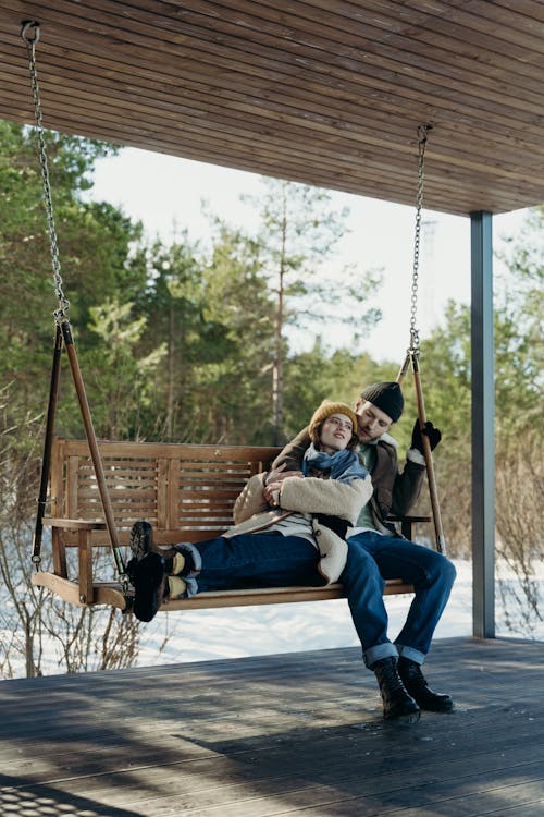 Free A Romantic Couple Sitting on a Wooden Swing while Embracing Stock Photo