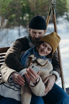 Smiling couple cuddling and looking at smartphone on a winter day outdoors.