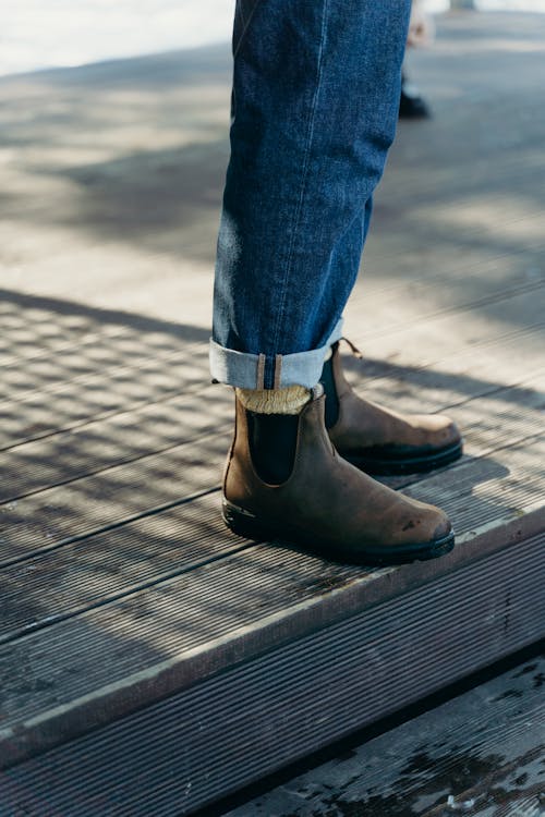 Free A Person in Blue Denim Jeans and Brown Leather Boots Standing on a Wooden Floor Stock Photo