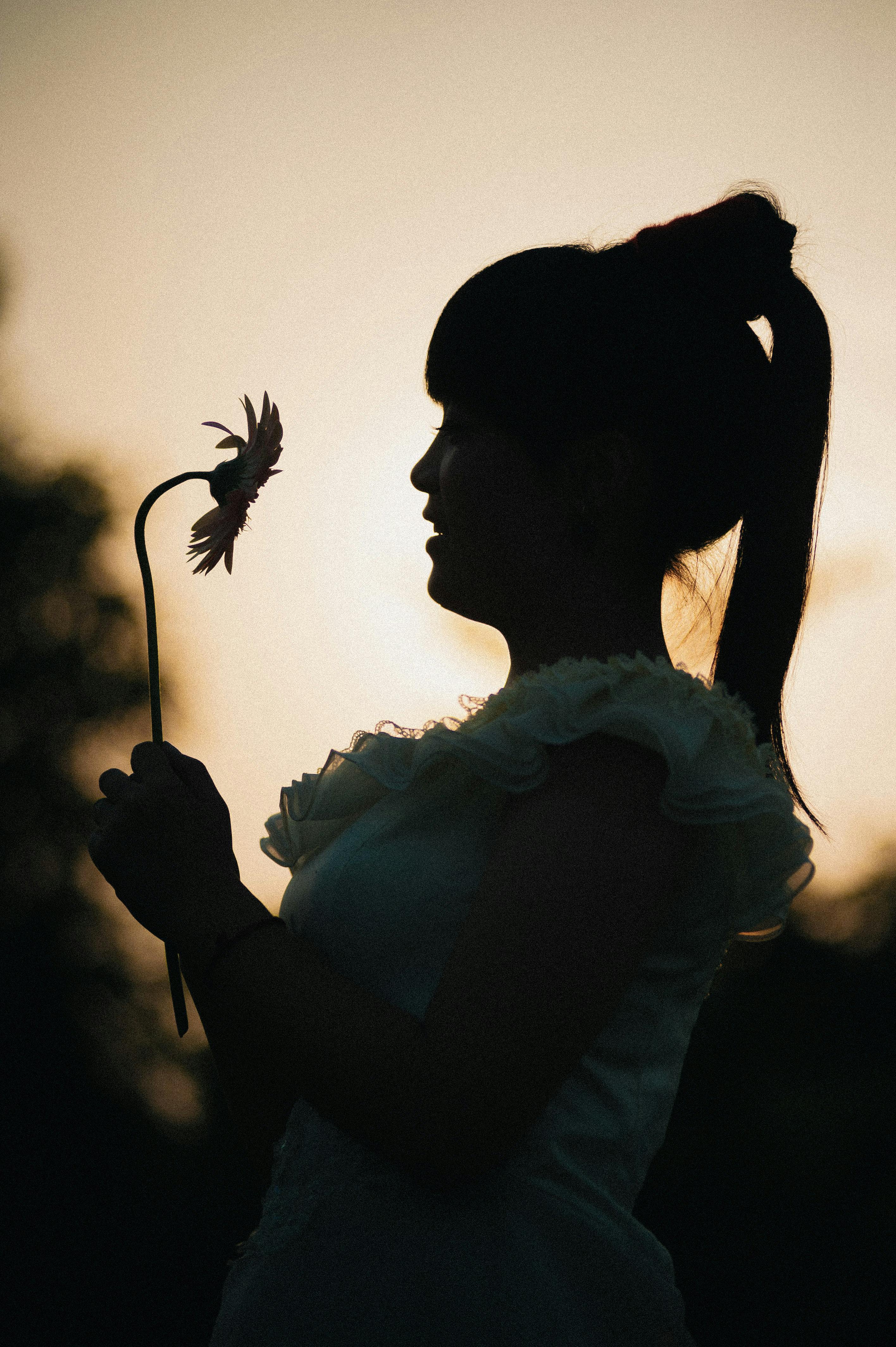 Silhouette of a woman holding a flower against a sunset backdrop, creating a serene scene.