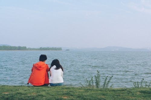 A Couple Sitting on Green Grass Field Near the Sea