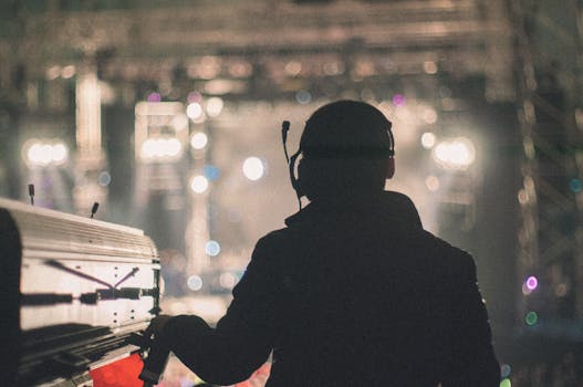 Sound engineer managing audio equipment at a live concert in Wuhan, silhouetted against bright stage lights.