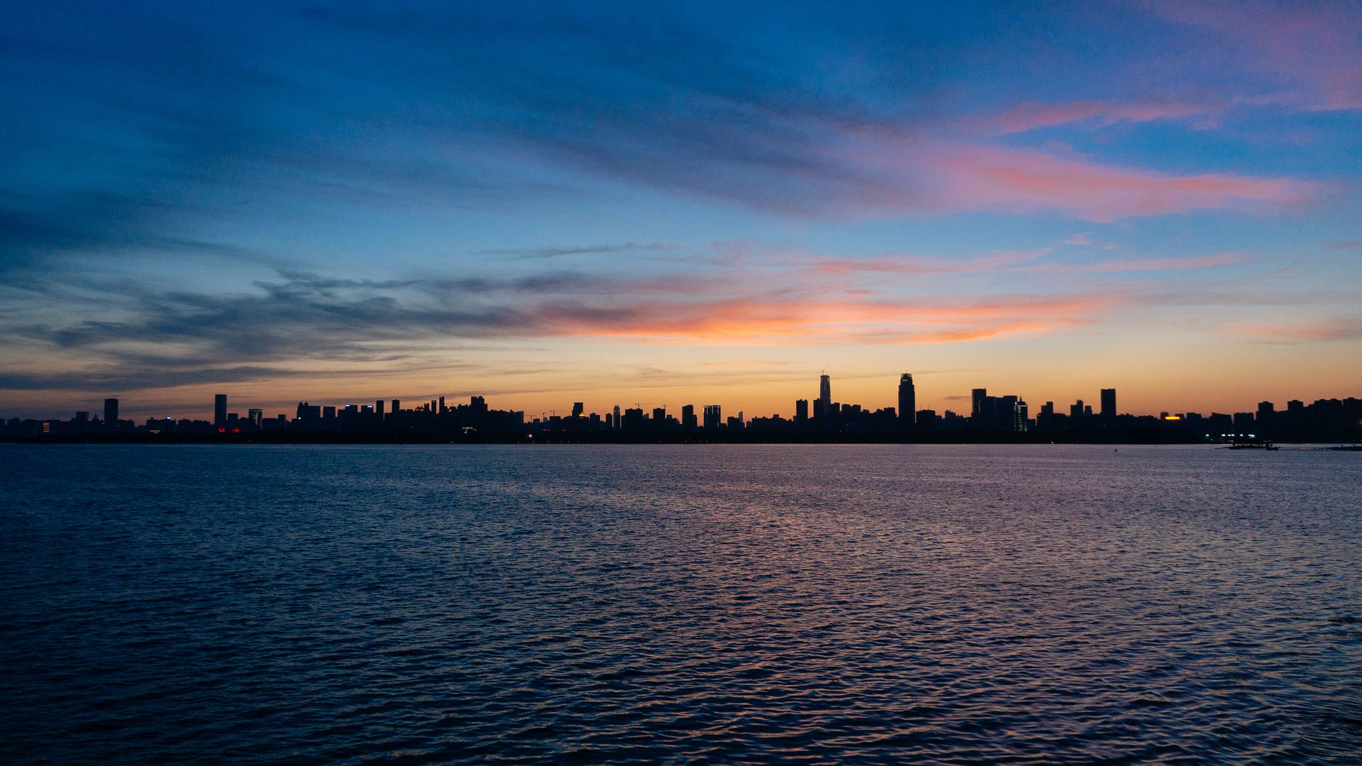 The serene skyline of Wuhan silhouetted against a twilight sky over a calm river.