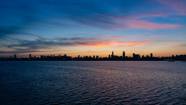 The serene skyline of Wuhan silhouetted against a twilight sky over a calm river.