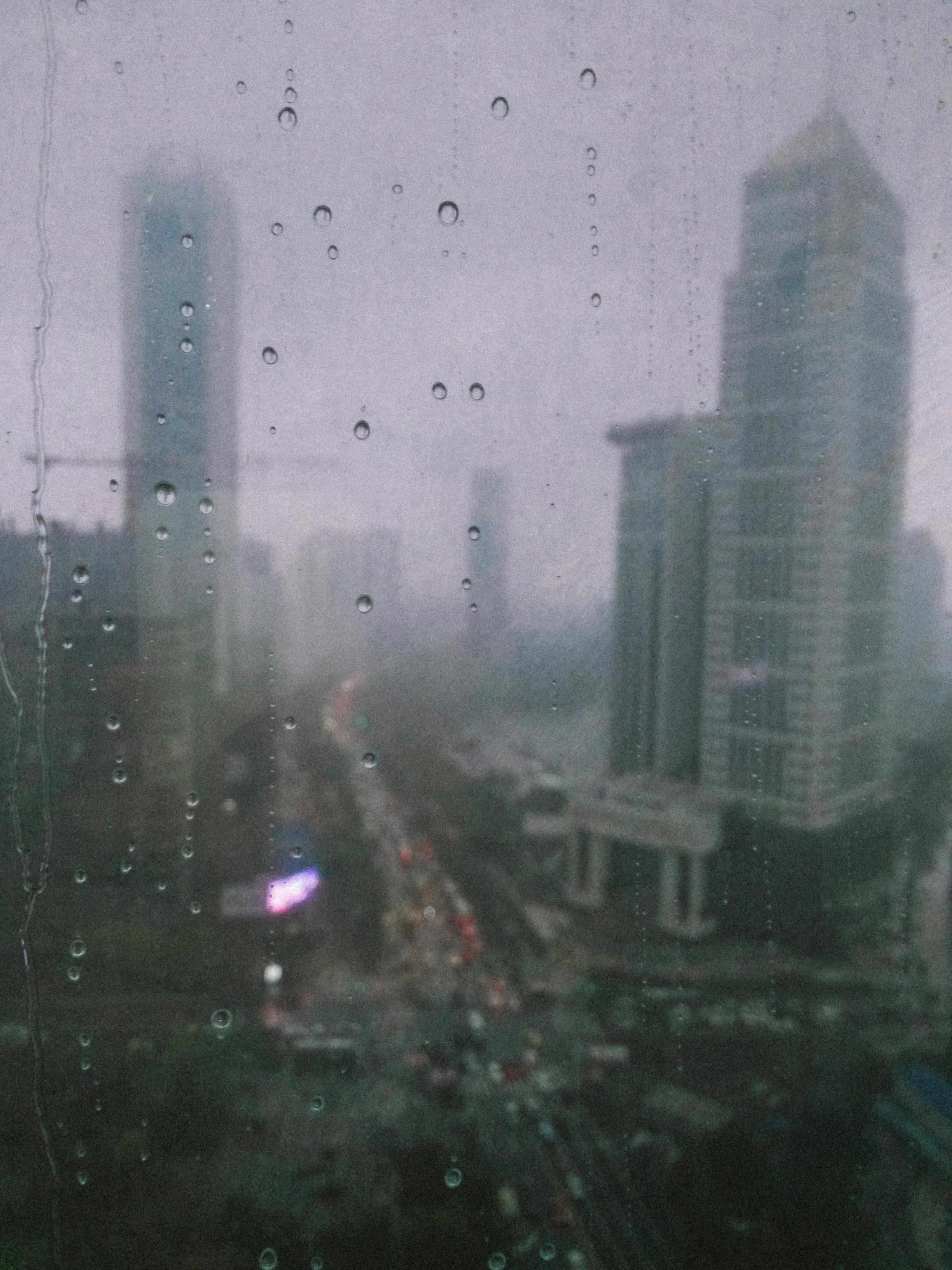 Raindrops on window with blurred Wuhan cityscape view, capturing urban life in rain.