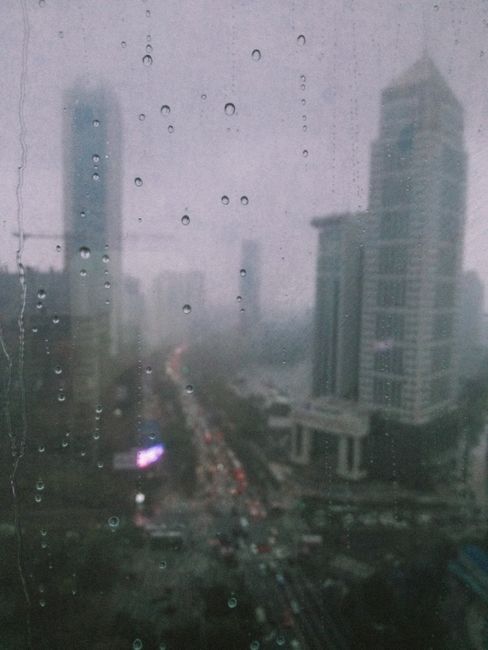 Raindrops on window with blurred Wuhan cityscape view, capturing urban life in rain.