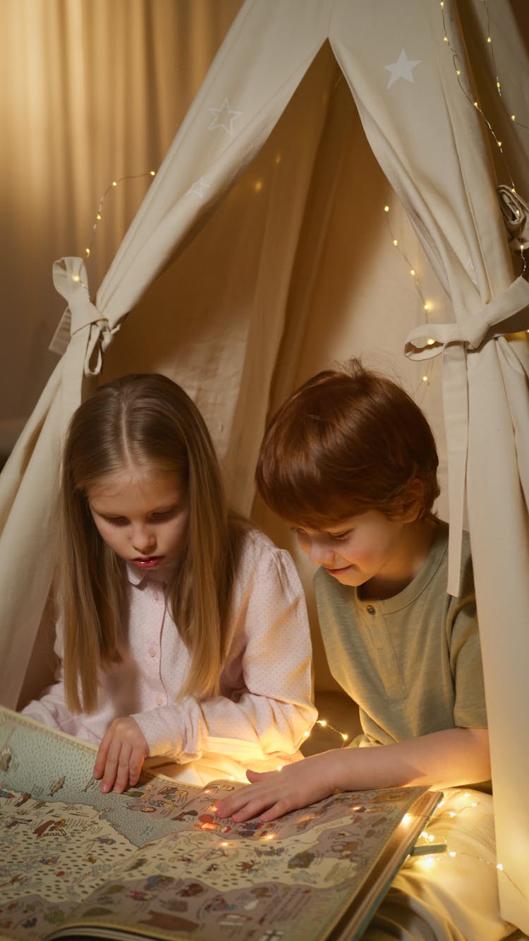 
Children Reading A Book While Inside An Indoor Tent