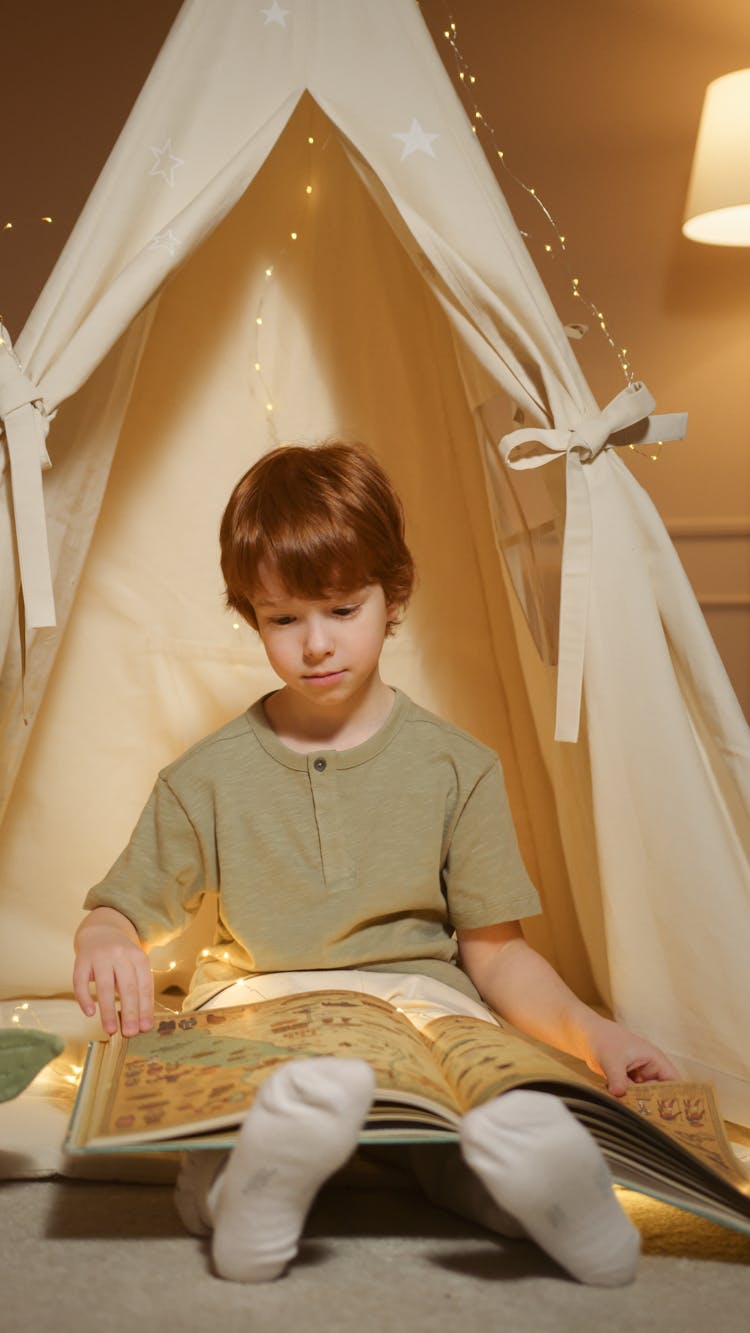 A Boy Reading A Book While Sitting In An Indoor Tent