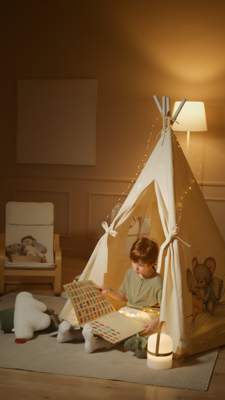 A Boy Reading A Book While Sitting In An Indoor Tent