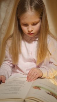 A young girl in pajamas quietly reads a book indoors, creating a serene and cozy atmosphere.
