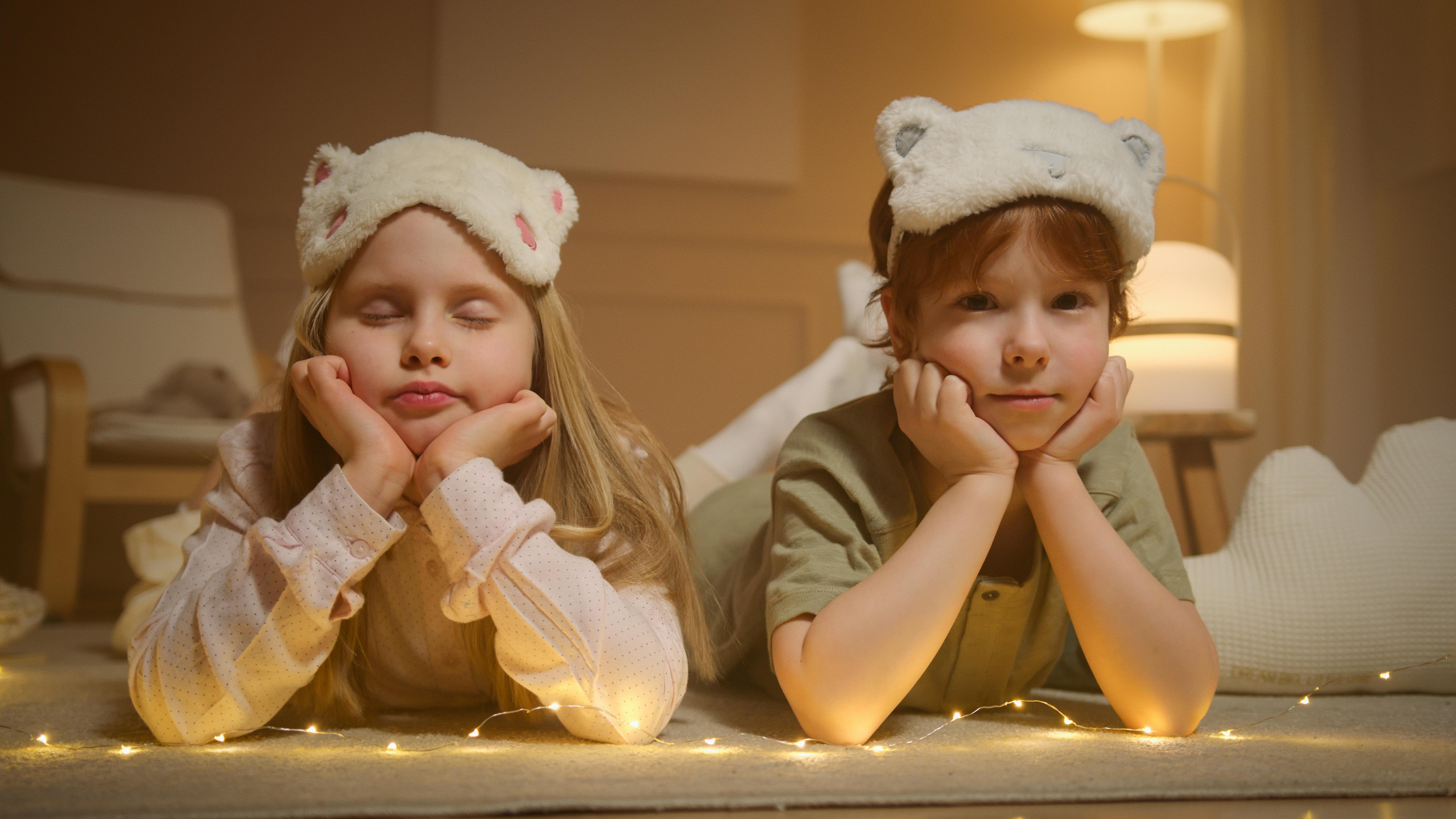 siblings wearing sleep masks lying on their bellies while posing