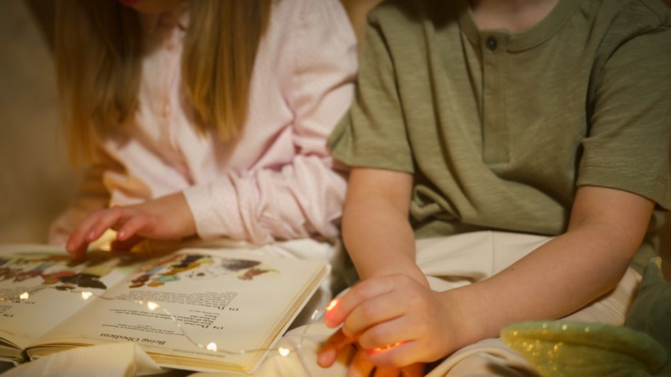 Dve deti čítajú rozprávku pod teplými svetielkami