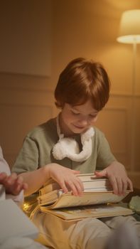 A happy child sits indoors with a stack of books, enjoying reading time in a warm setting.