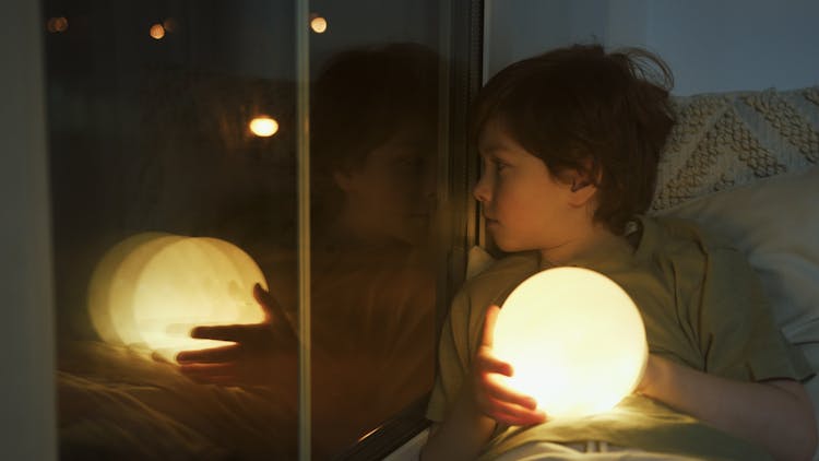 A Boy Holding A Glowing Ball While Looking Through The Window