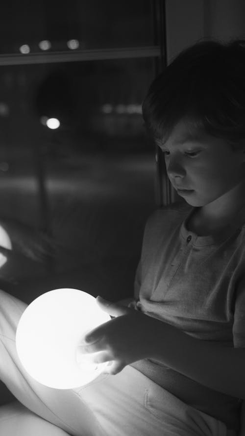 Grayscale Photo of Boy Holding A Glowing Round Lamp