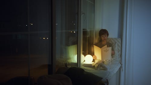 Free A Boy Reading a Book while Sitting on a Windowsill Stock Photo