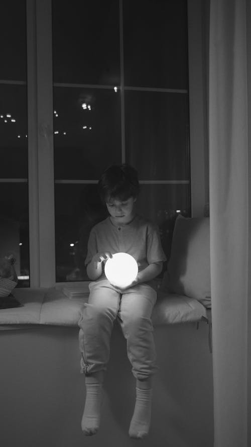 Grayscale Photograph of a Boy Holding a Light Ball