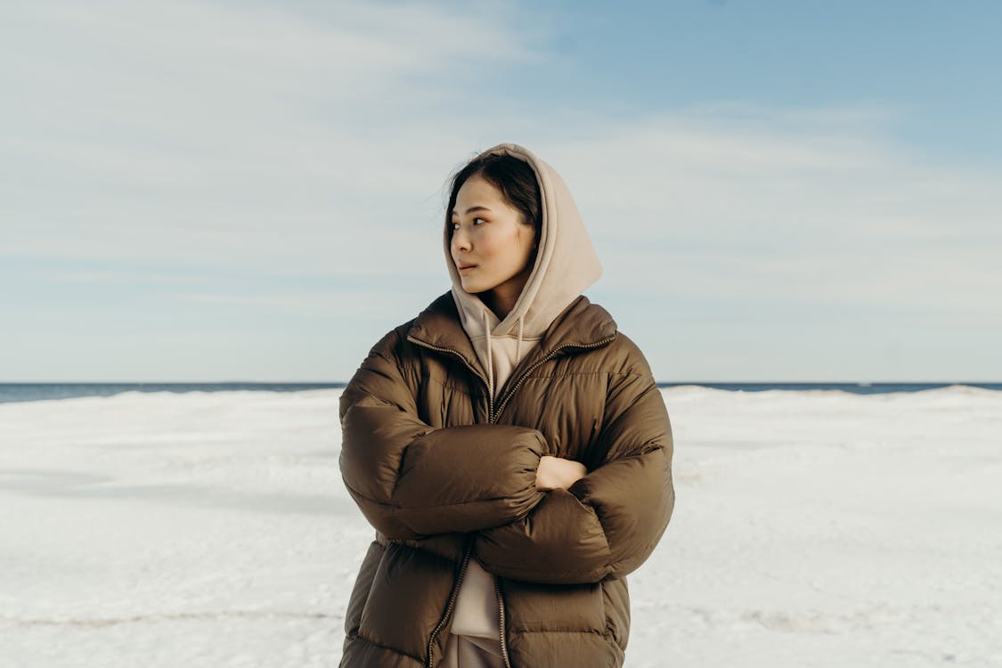 Free Woman in Brown Winter Coat Standing on Snow Covered Field Stock Photo