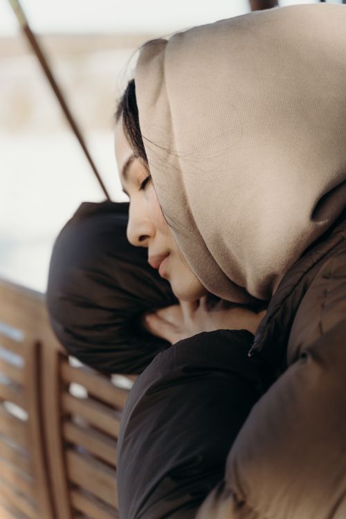Free Close-up of an Asian woman in a puffer jacket with eyes closed, enjoying a serene moment outdoors. Stock Photo
