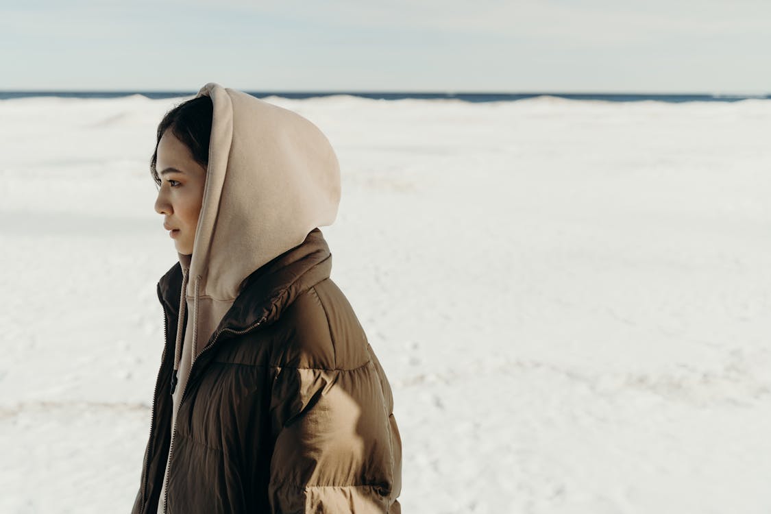 Woman in Brown Hoodie and Brown Puffer Jacket Standing On Snow
