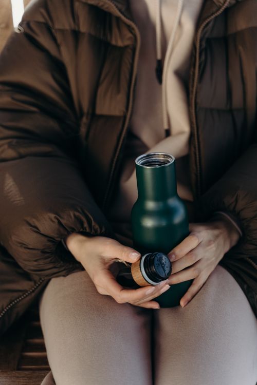 Free Person in winter clothing holding a thermos, highlighting warmth and coziness. Stock Photo
