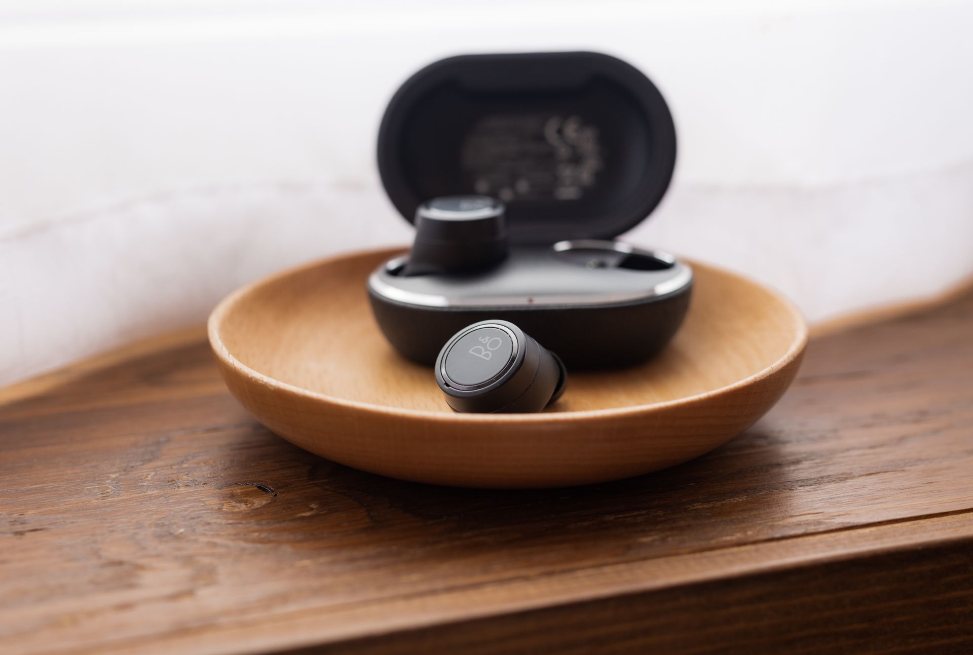 Black wireless earbuds placed in a wooden bowl on a brown wooden surface, showcasing modern technology.