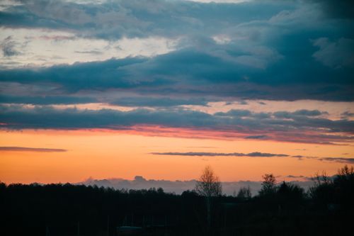 Free A stunning sunset featuring a colorful sky above a silhouette of trees and rolling hills. Stock Photo