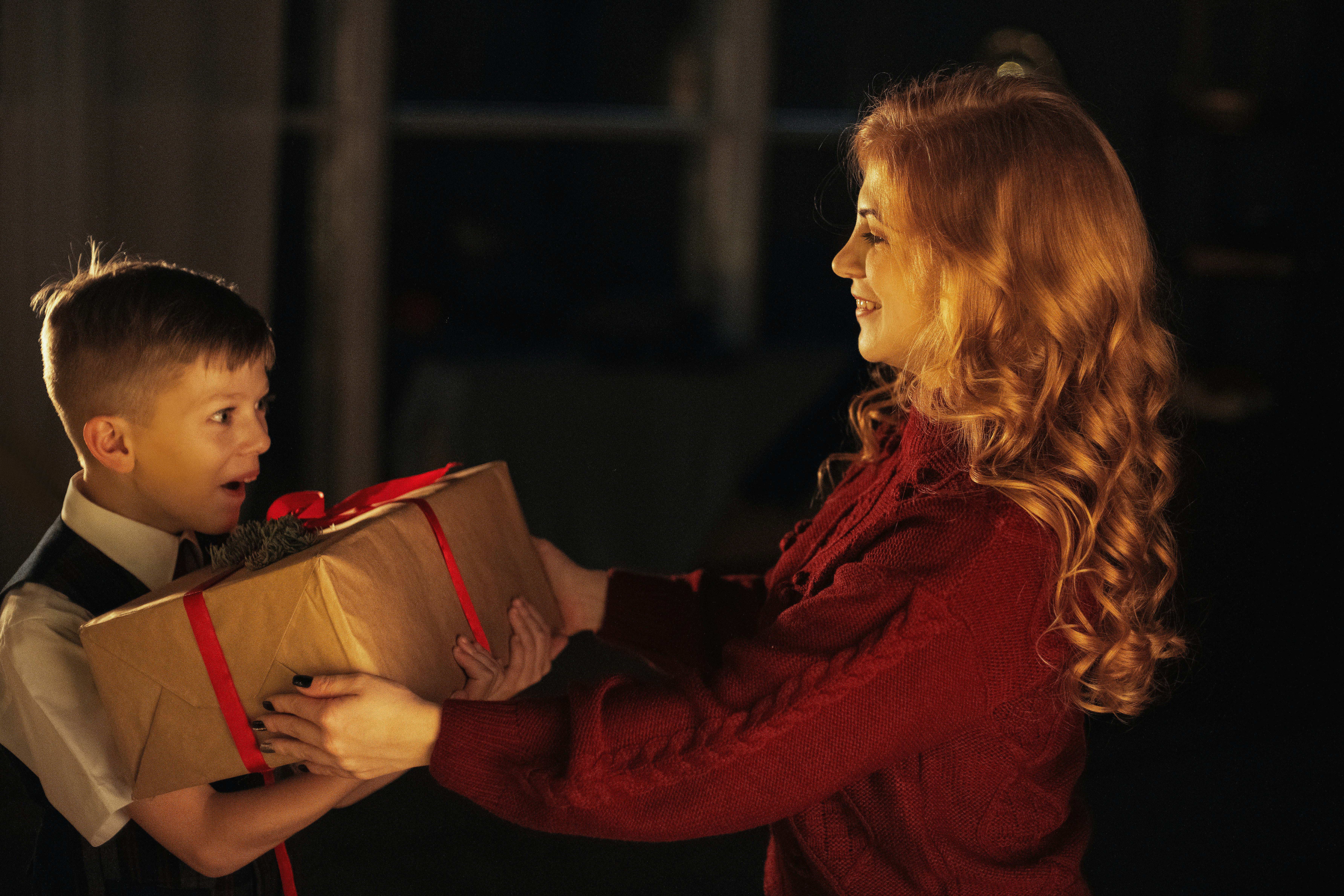 A mother gives her son a surprise holiday gift indoors. Joyful family moment.