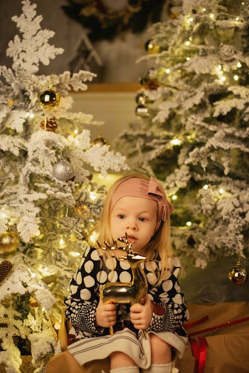 Girl in Black and White Polka Dot Shirt Sitting Beside A Christmas Tree