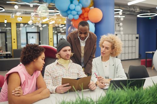 Free Diverse office team collaborating on a project with laptops and notebooks in an open, modern workspace. Stock Photo