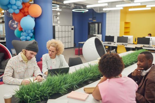 Diverse team collaborating creatively in a modern, colorful office workspace with laptops and vibrant decor.