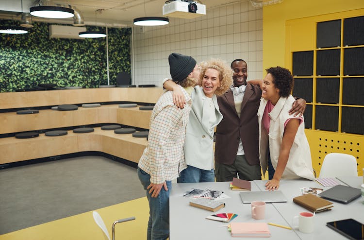 A Group Of People Standing Beside A Desk Hugging